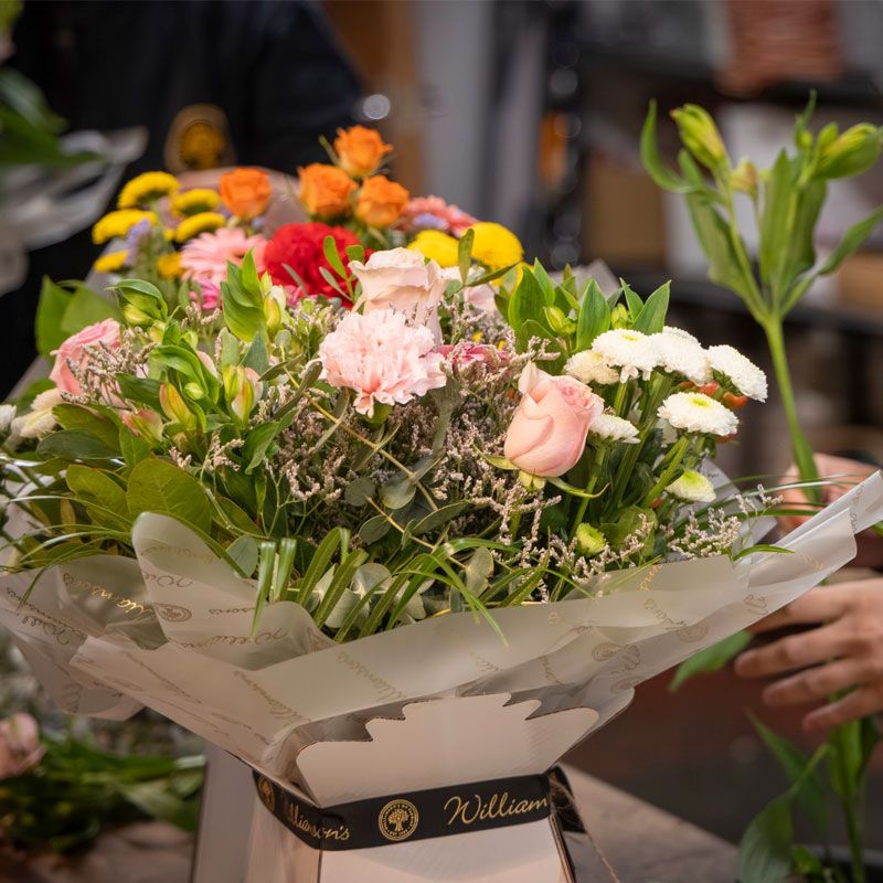 Fresh flower bouquet of pink, red, yellow, and white flowers being arranged by a Williamson's florist