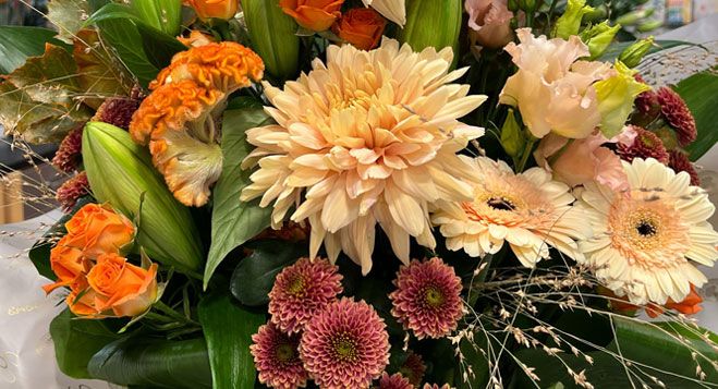 Luxurious autumn flower arrangement featuring chrysanthemums, dahlias, gerberas, and roses in warm orange, peach, and pink shades