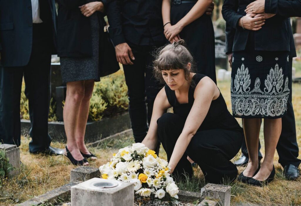 Mourning family placing Christmas memorial flowers of white and yellow on a grace.