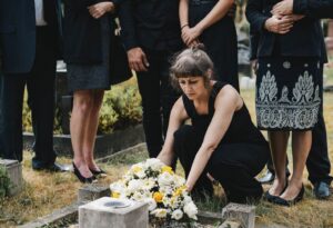 Mourning family placing Christmas memorial flowers of white and yellow on a grace.