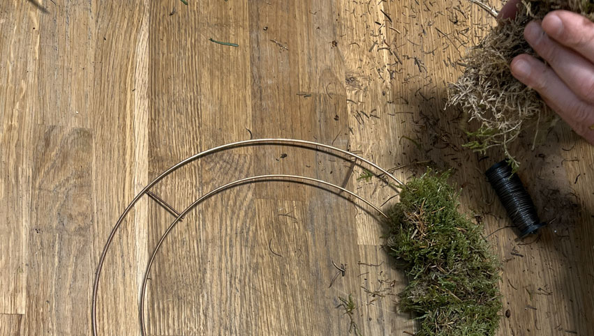 Clusters of fresh moss being added to a flower wreath base.